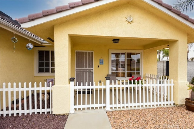 view of front of house featuring a porch, a tiled roof, a fenced front yard, and stucco siding