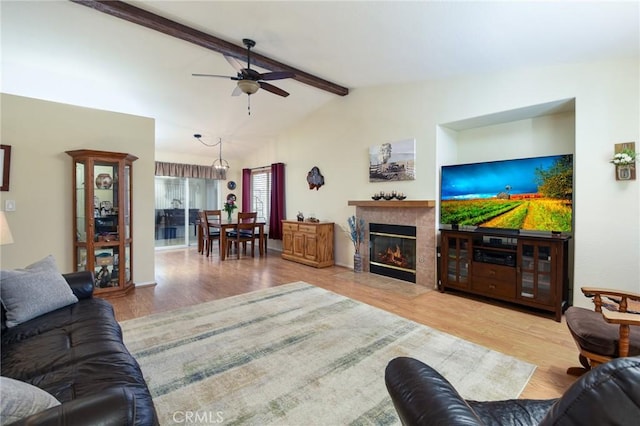 living area with vaulted ceiling with beams, ceiling fan, wood finished floors, and a tile fireplace