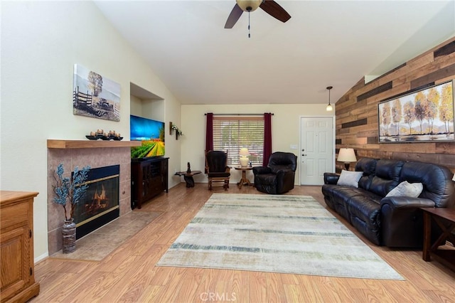 living room featuring a tiled fireplace, light wood-style floors, a ceiling fan, and vaulted ceiling