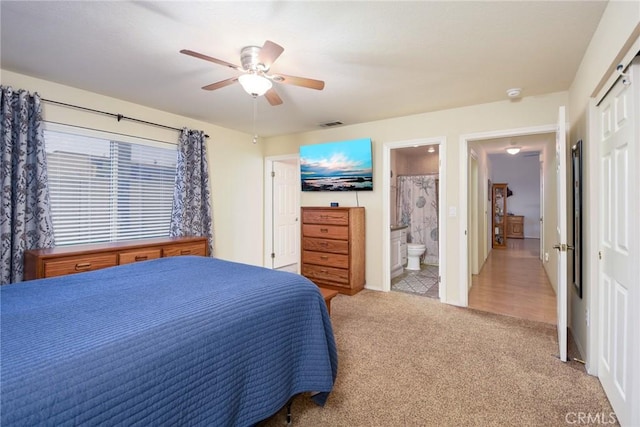 carpeted bedroom featuring a closet, visible vents, baseboards, ensuite bathroom, and ceiling fan