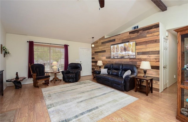living area featuring wood walls, lofted ceiling with beams, light wood-type flooring, and visible vents