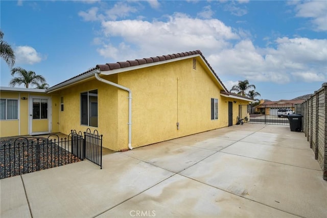 view of side of property with stucco siding, a gate, fence, and concrete driveway