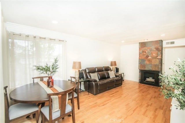 living room with crown molding, a tile fireplace, visible vents, and light wood-type flooring