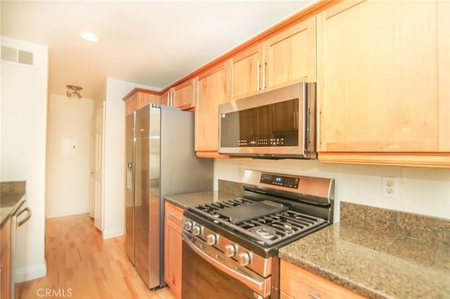 kitchen featuring light brown cabinetry, light stone countertops, light wood-style flooring, stainless steel appliances, and visible vents