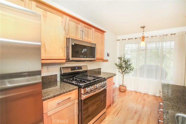 kitchen featuring pendant lighting, light brown cabinetry, light wood-style floors, dark stone countertops, and appliances with stainless steel finishes