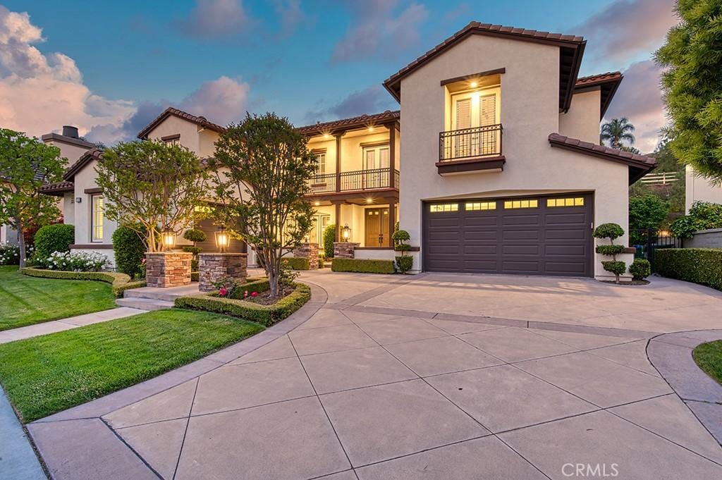 mediterranean / spanish house featuring a yard, a balcony, concrete driveway, an attached garage, and stucco siding