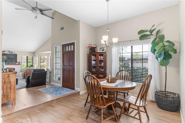 dining area with high vaulted ceiling, ceiling fan with notable chandelier, light wood-type flooring, and visible vents