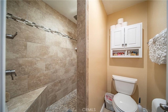 bathroom featuring baseboards, a tile shower, and toilet