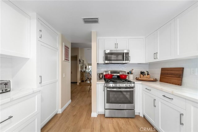 kitchen with tasteful backsplash, stainless steel appliances, light wood-type flooring, and visible vents