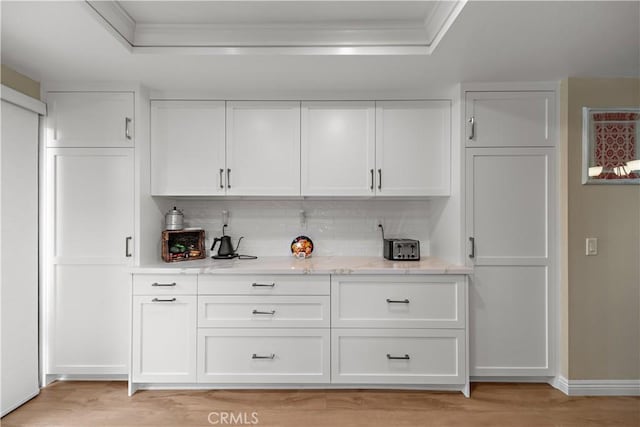 bar featuring crown molding, baseboards, a tray ceiling, tasteful backsplash, and light wood finished floors