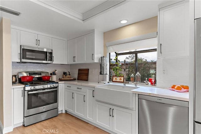 kitchen with visible vents, tasteful backsplash, light countertops, stainless steel appliances, and white cabinetry