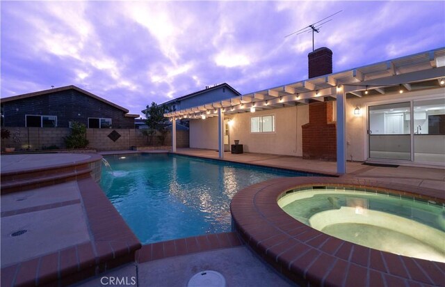 pool at dusk featuring fence, a pool with connected hot tub, and a patio area