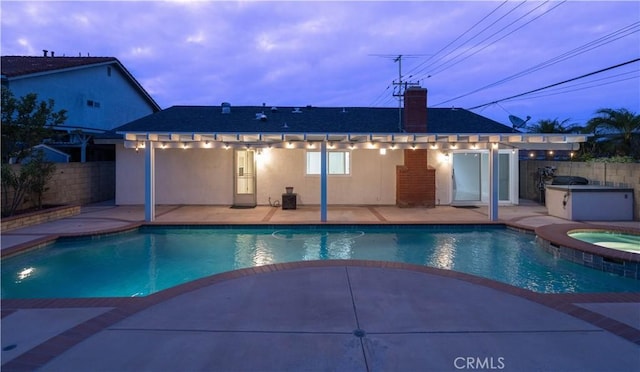 pool at dusk with a patio, an outdoor kitchen, a fenced backyard, and a pool with connected hot tub