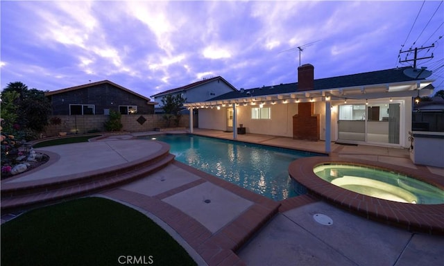 pool at dusk with a pool with connected hot tub, a patio area, and fence