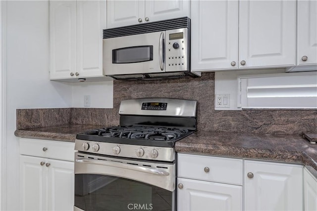 kitchen featuring stainless steel appliances, dark countertops, white cabinetry, and backsplash