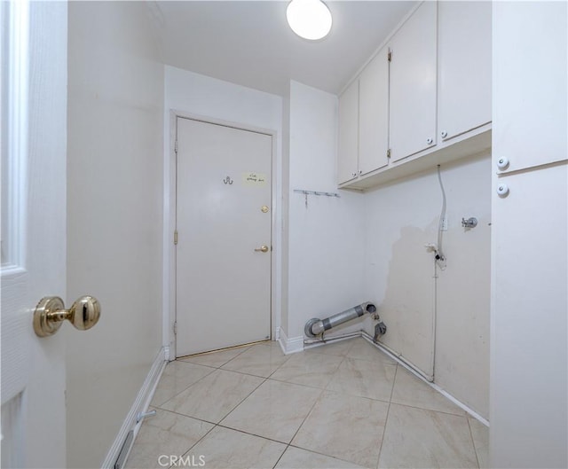 clothes washing area featuring cabinet space, light tile patterned flooring, and baseboards