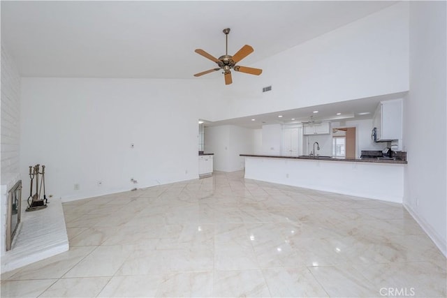 unfurnished living room featuring a ceiling fan, high vaulted ceiling, a sink, and light marble finish flooring