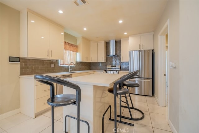 kitchen featuring a kitchen bar, visible vents, stove, freestanding refrigerator, and wall chimney exhaust hood