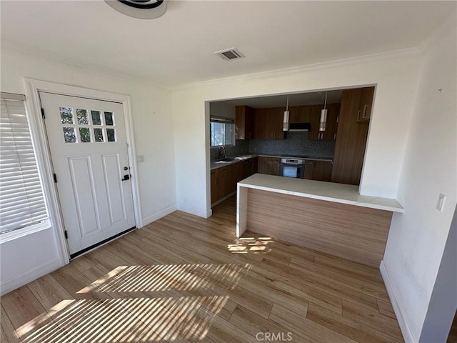 kitchen with decorative backsplash, a peninsula, black oven, baseboards, and light wood-style flooring