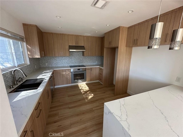 kitchen featuring a sink, under cabinet range hood, light stone countertops, and oven