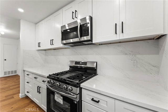 kitchen featuring appliances with stainless steel finishes, tasteful backsplash, white cabinetry, and visible vents