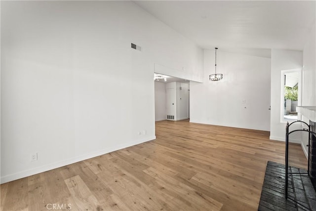 unfurnished living room featuring a notable chandelier, high vaulted ceiling, visible vents, and light wood-style floors