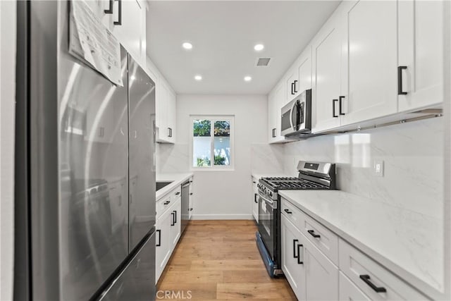kitchen featuring light wood-style floors, appliances with stainless steel finishes, white cabinetry, and visible vents