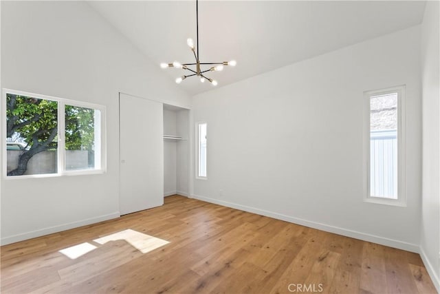interior space with light wood-style floors, high vaulted ceiling, a chandelier, baseboards, and a closet