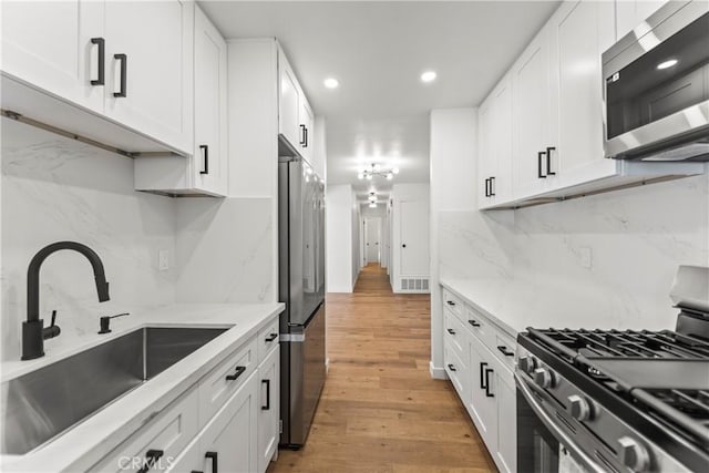 kitchen with appliances with stainless steel finishes, a sink, light wood finished floors, white cabinetry, and decorative backsplash