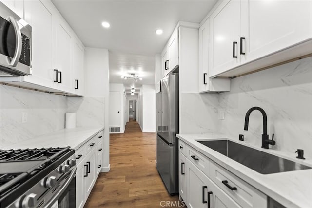 kitchen with appliances with stainless steel finishes, dark wood finished floors, a sink, recessed lighting, and white cabinetry