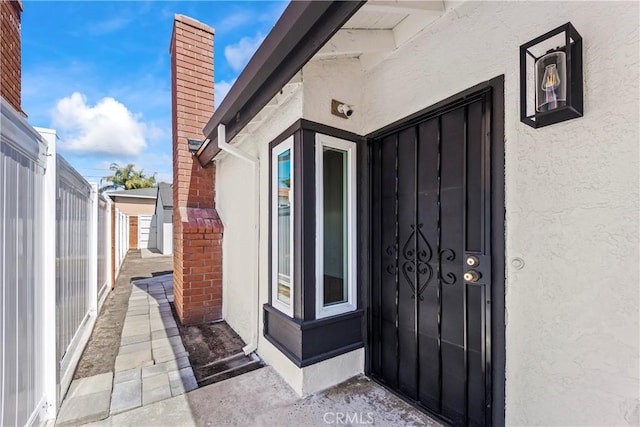 property entrance featuring fence, stucco siding, and a chimney