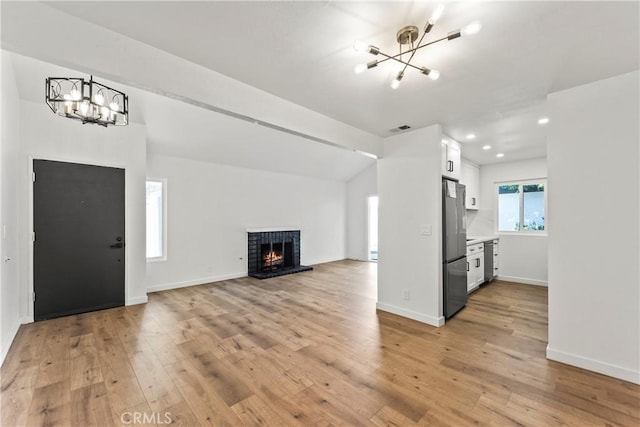 unfurnished living room featuring light wood-style floors, visible vents, a fireplace, and a notable chandelier