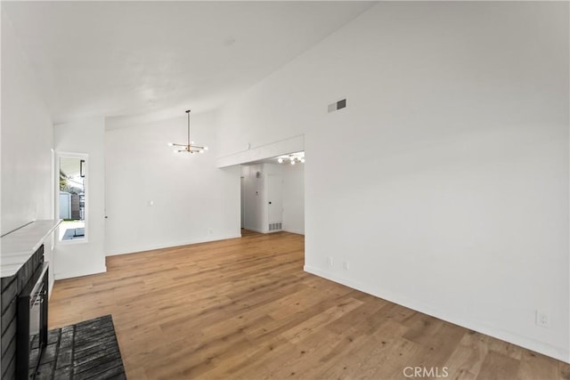 unfurnished living room with a notable chandelier, visible vents, high vaulted ceiling, and light wood-style floors
