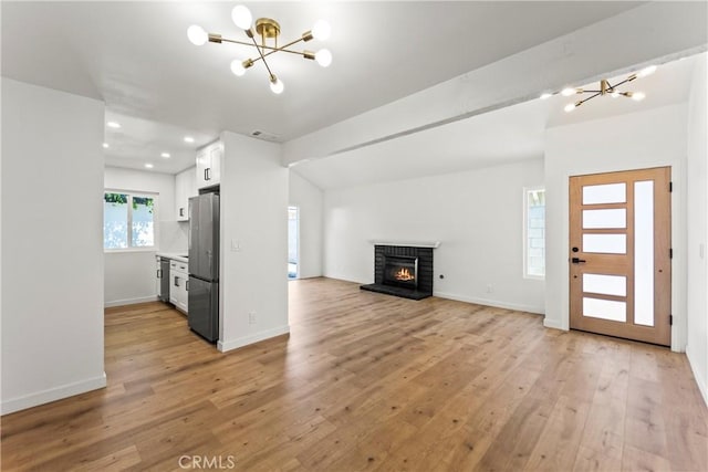 unfurnished living room with a brick fireplace, recessed lighting, light wood-style flooring, and a chandelier