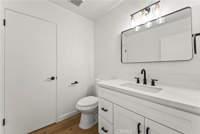 half bath with vanity, toilet, wood finished floors, and visible vents