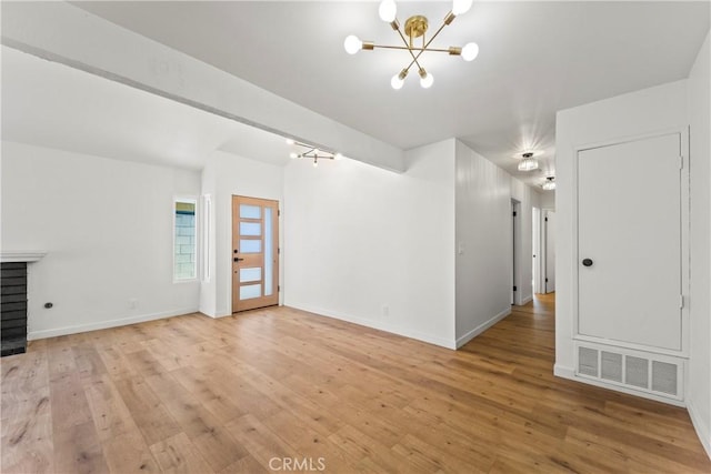 unfurnished living room featuring an inviting chandelier, light wood-style flooring, baseboards, and visible vents