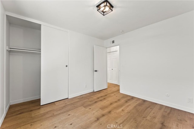 unfurnished bedroom with baseboards, a closet, wood finished floors, and visible vents