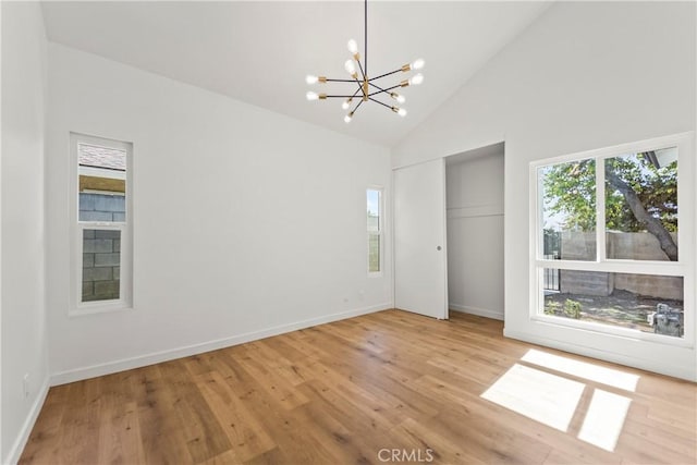 spare room featuring high vaulted ceiling, baseboards, light wood-type flooring, and a notable chandelier