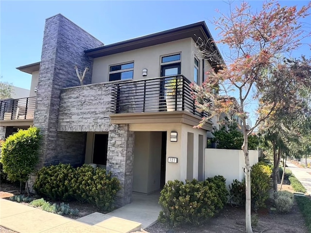 contemporary home featuring fence, a balcony, stone siding, and stucco siding