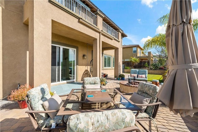 view of patio featuring a balcony, fence, outdoor dining area, and an outdoor living space with a fire pit