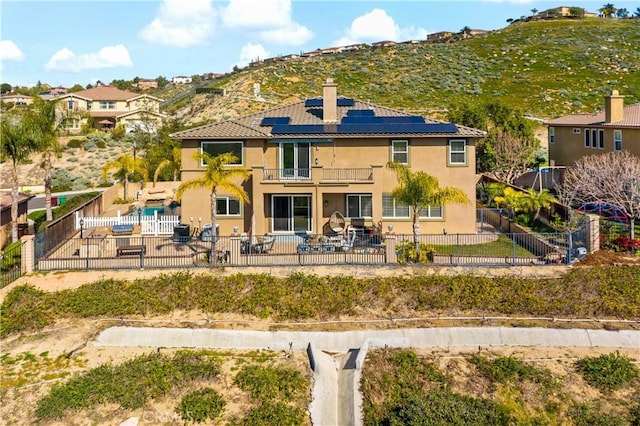 rear view of house with a fenced backyard, a patio, solar panels, and a balcony