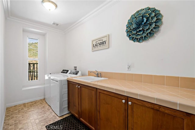 laundry area featuring crown molding, washing machine and dryer, cabinet space, a sink, and baseboards