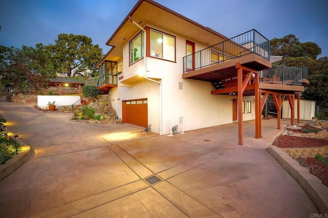 back of house with an attached garage, stucco siding, driveway, and a deck