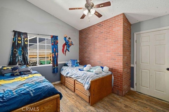 bedroom featuring brick wall, light wood-style floors, a textured ceiling, a ceiling fan, and vaulted ceiling