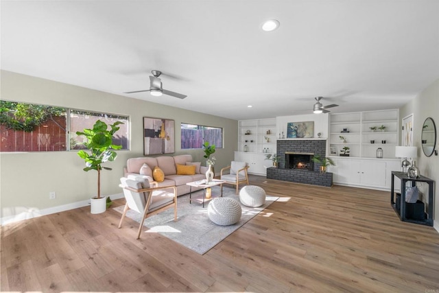 living room with ceiling fan, a brick fireplace, recessed lighting, baseboards, and wood finished floors