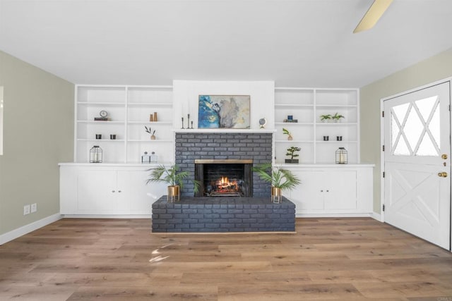 living area with baseboards, built in features, wood finished floors, and a fireplace