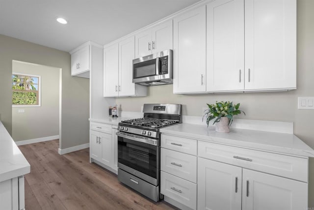 kitchen with white cabinets, stainless steel appliances, baseboards, recessed lighting, and wood finished floors