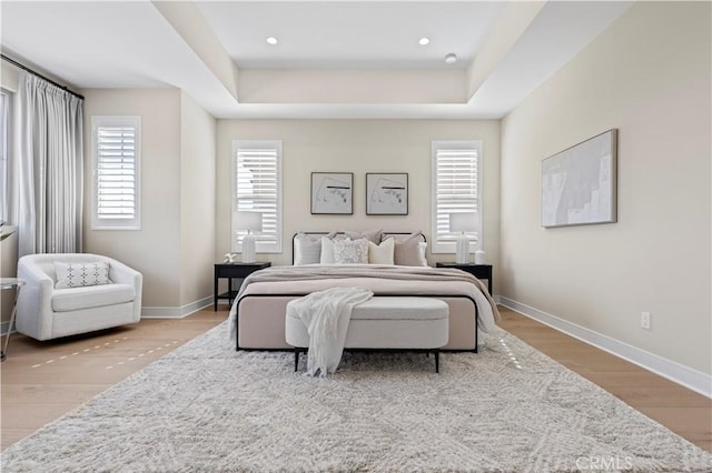bedroom featuring recessed lighting, baseboards, wood finished floors, and a tray ceiling