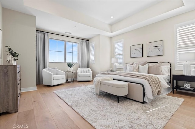bedroom with a raised ceiling, baseboards, light wood-style flooring, and visible vents