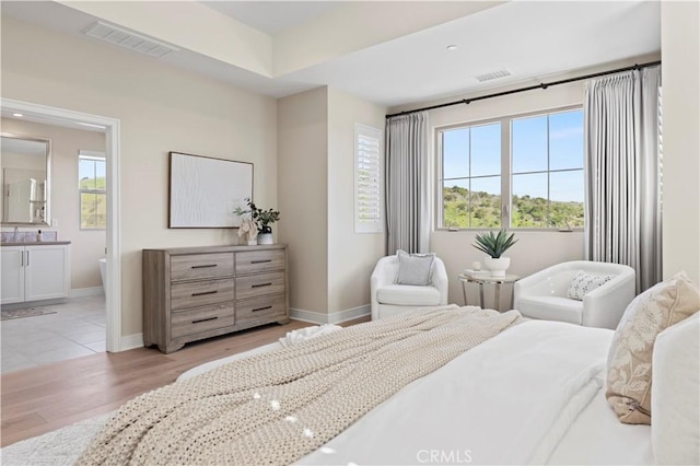 bedroom featuring baseboards, visible vents, light wood-style flooring, and ensuite bathroom